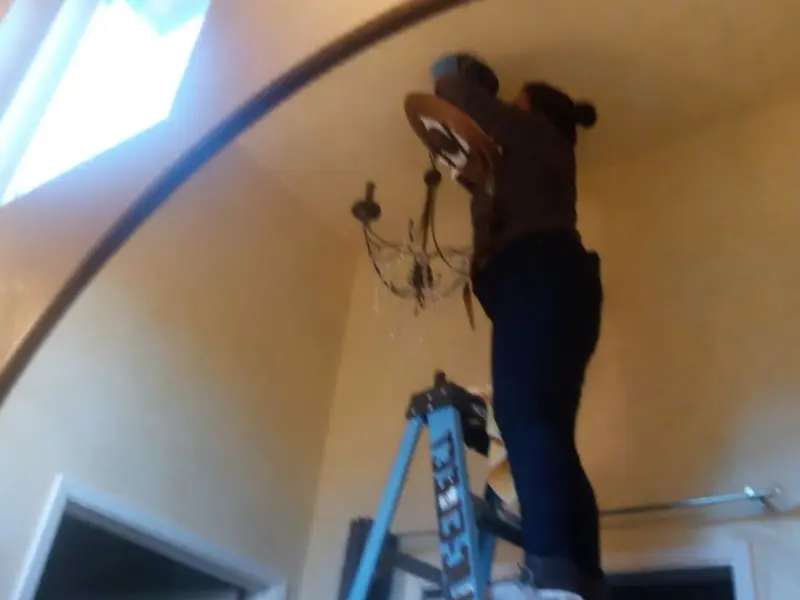 Electrician installing a chandelier in a Justice residence